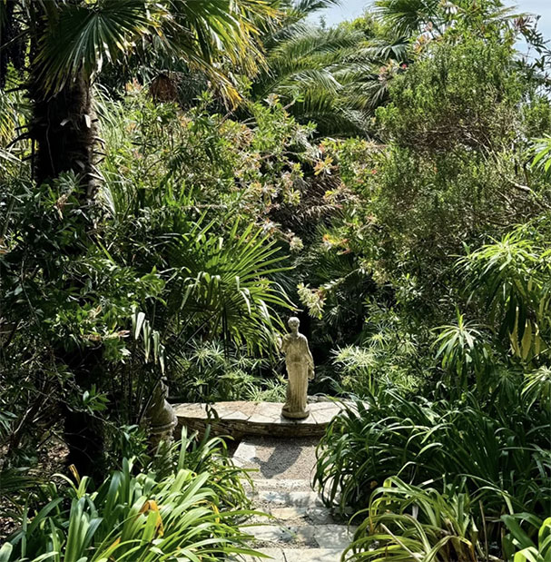 Serene space that has a statue at the bottom of a set of steps with palms and plants surrounding the space.